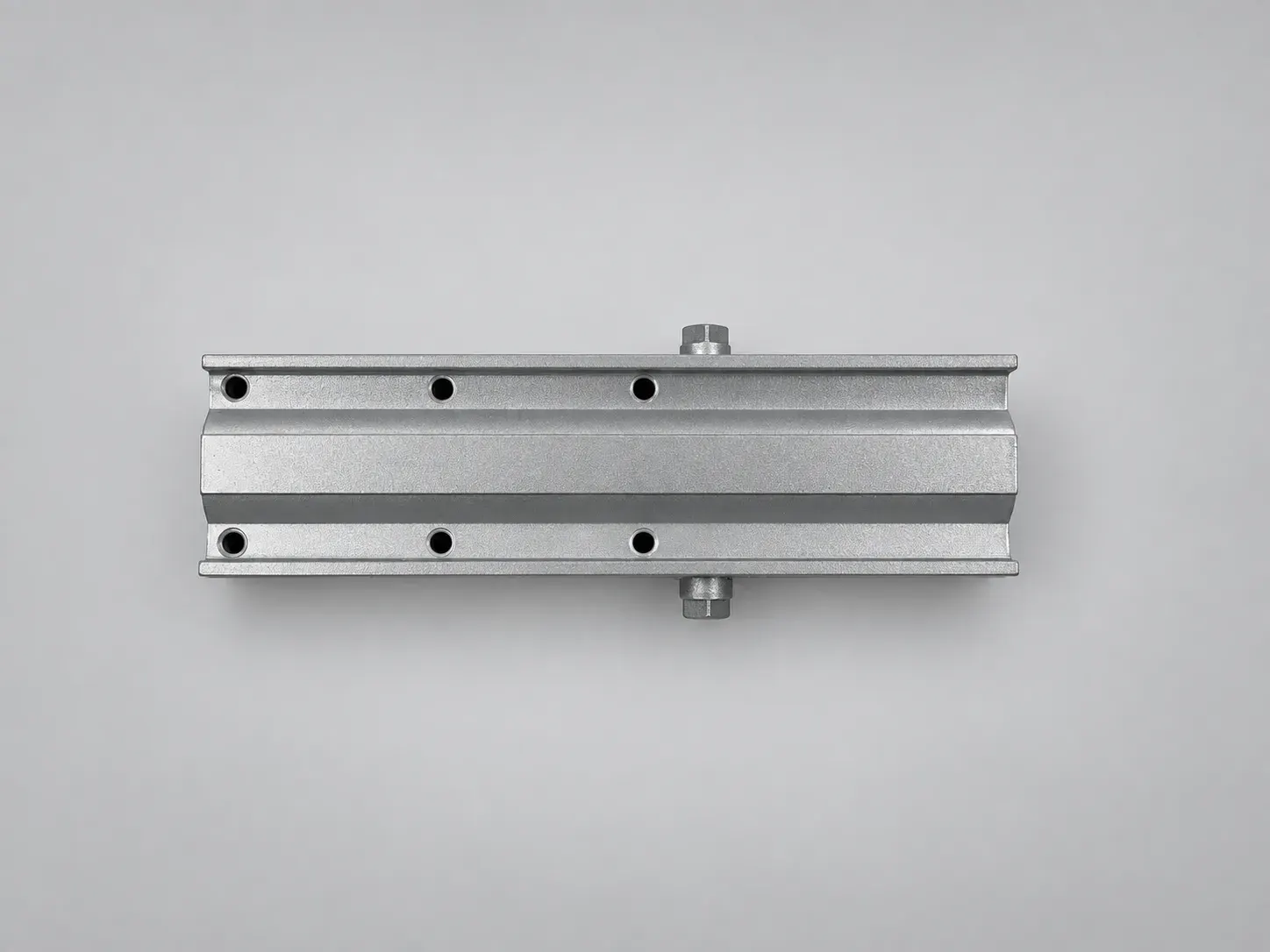 Extruded aluminium door closer body without its cover, machined face with six fixing holes and both pinion ends, overhead view, studio photograph